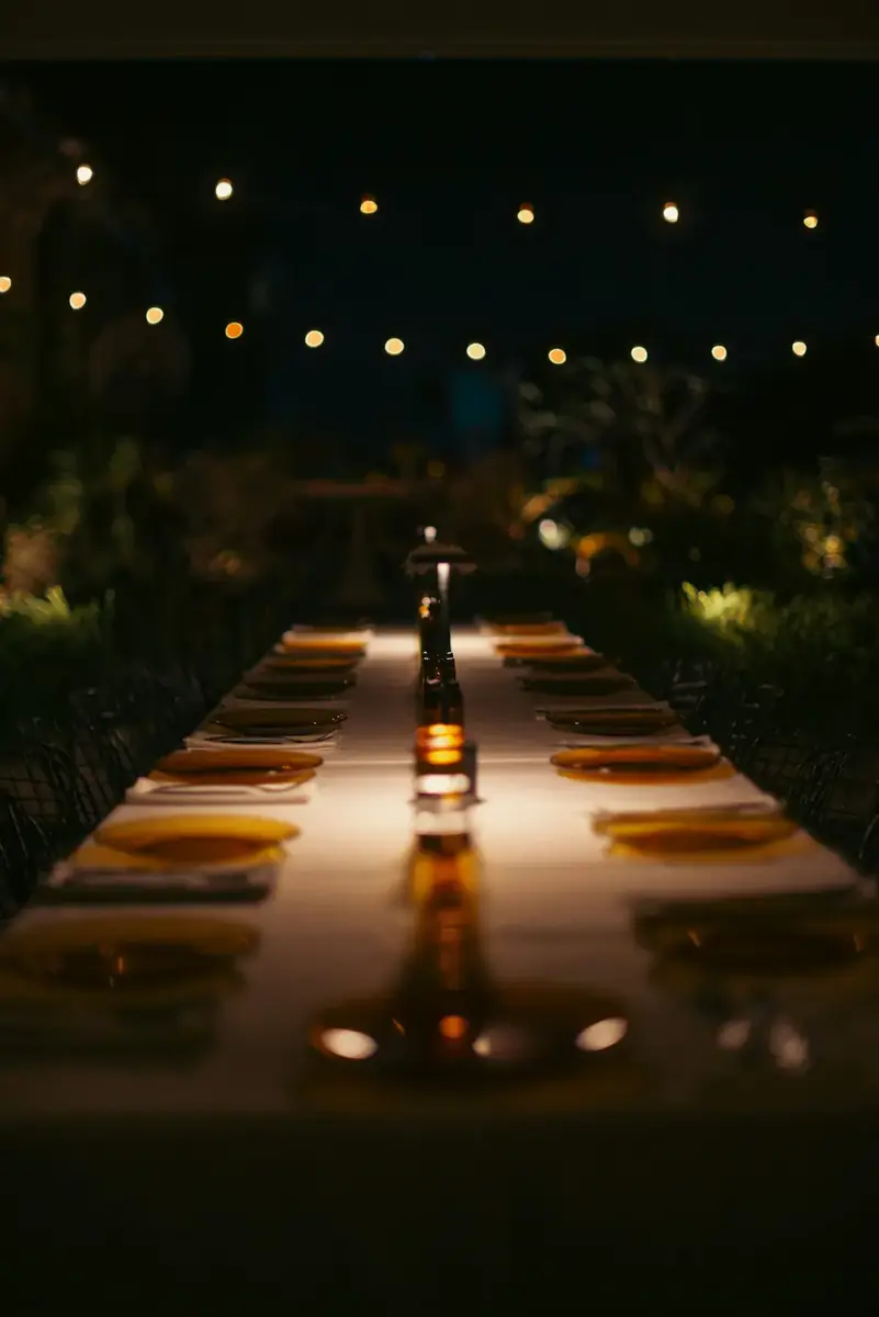 A long table set for a reception dinner under festoon lighting